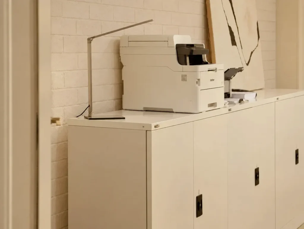 Commercial lawyers: white metal storage cabinets with a printer and desk lamp against a white brick wall in soft, warm light