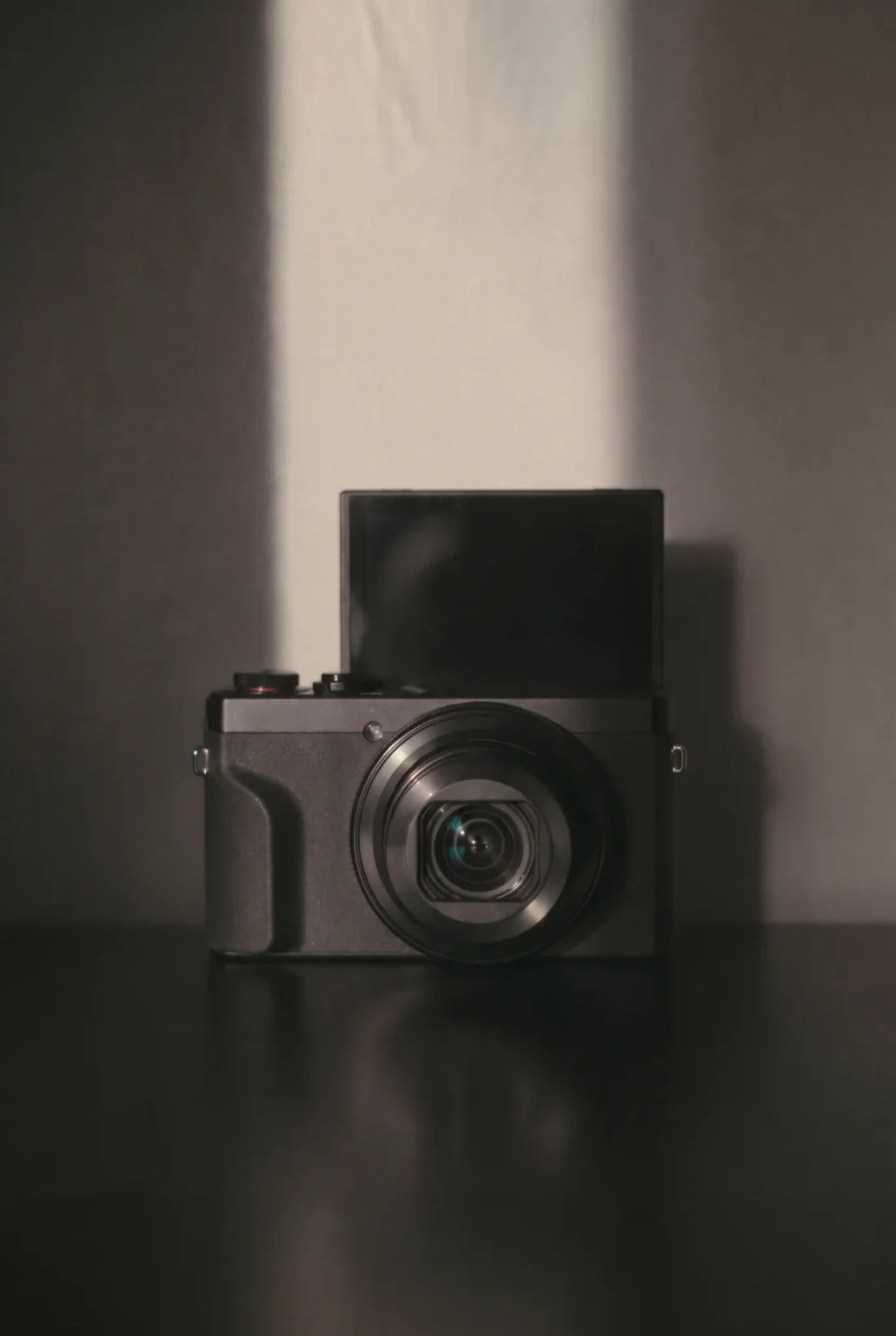 A modern compact camera against a softly lit wall