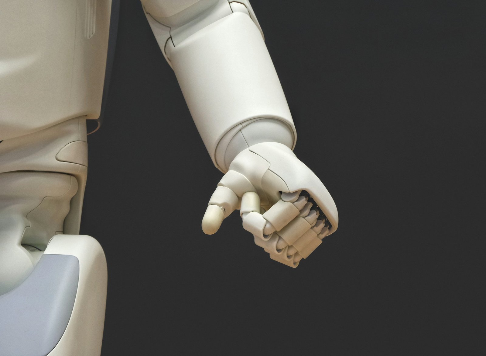 A white robotic hand reaching forward against a dark background